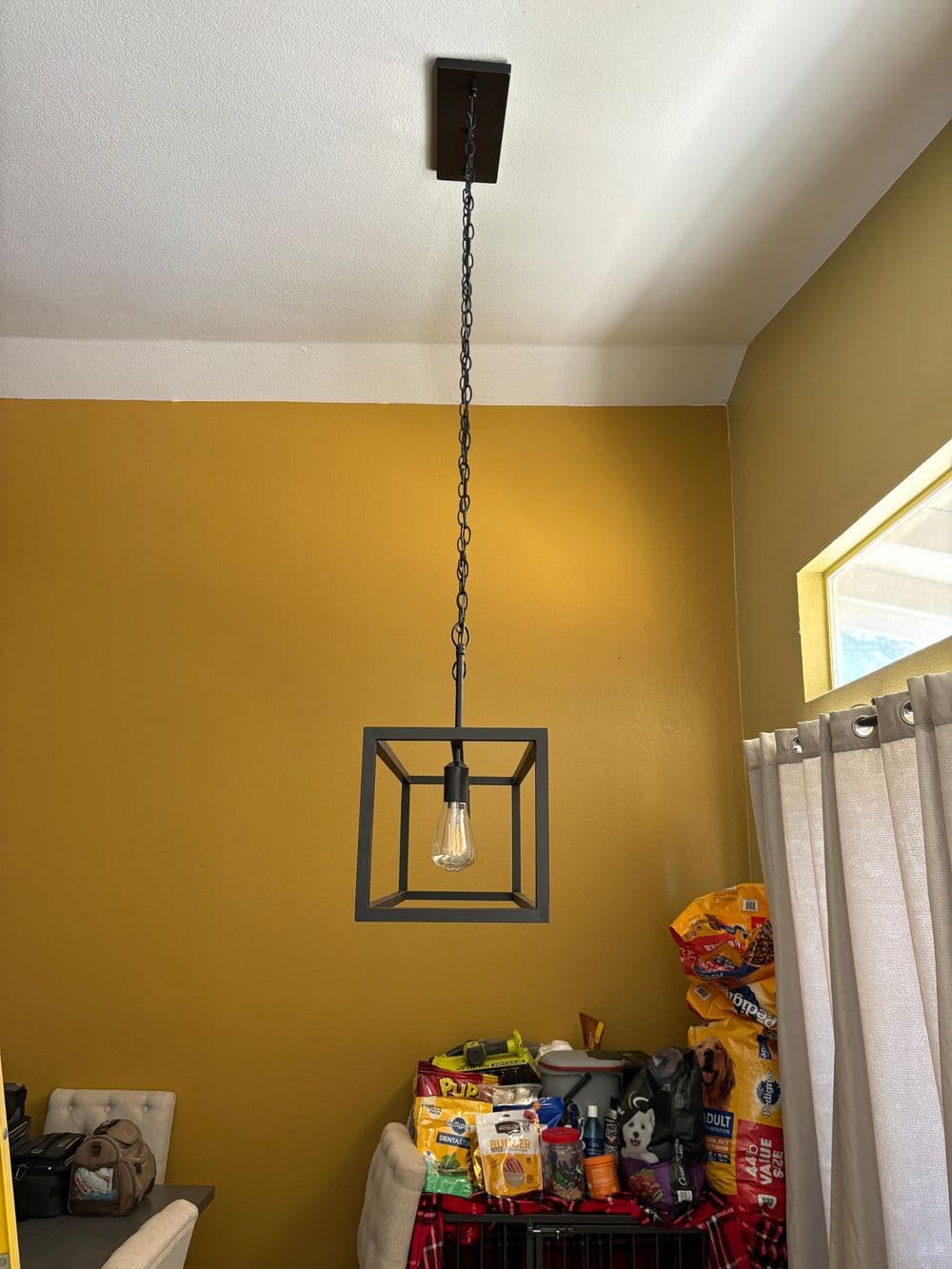 Modern pendant light fixture hanging from ceiling with a square frame and industrial bulb.