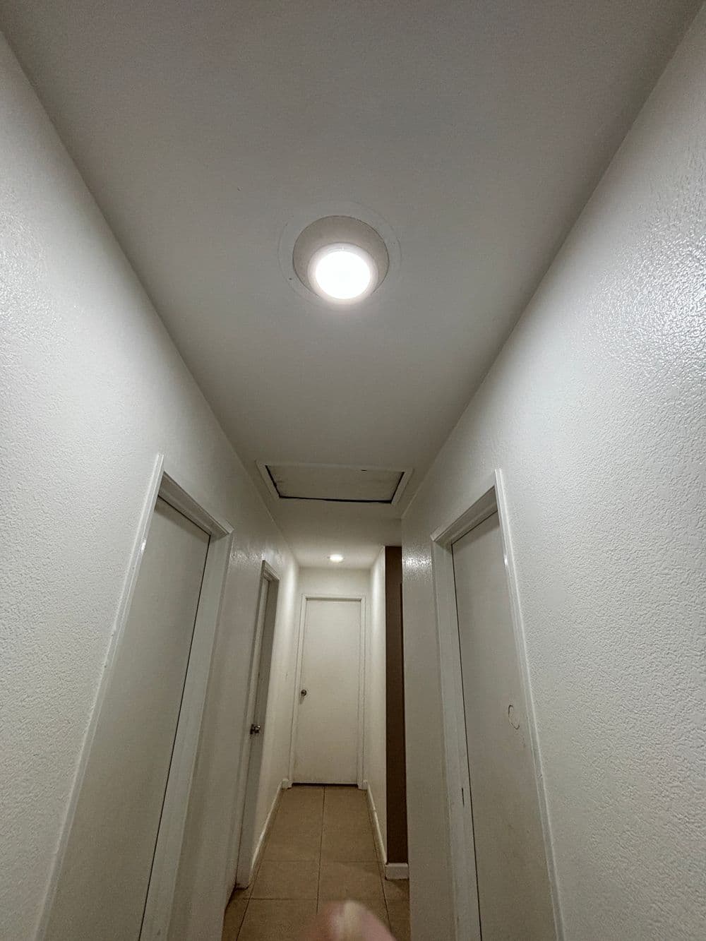 Bright hallway with white walls, doors on both sides, and a ceiling light fixture.
