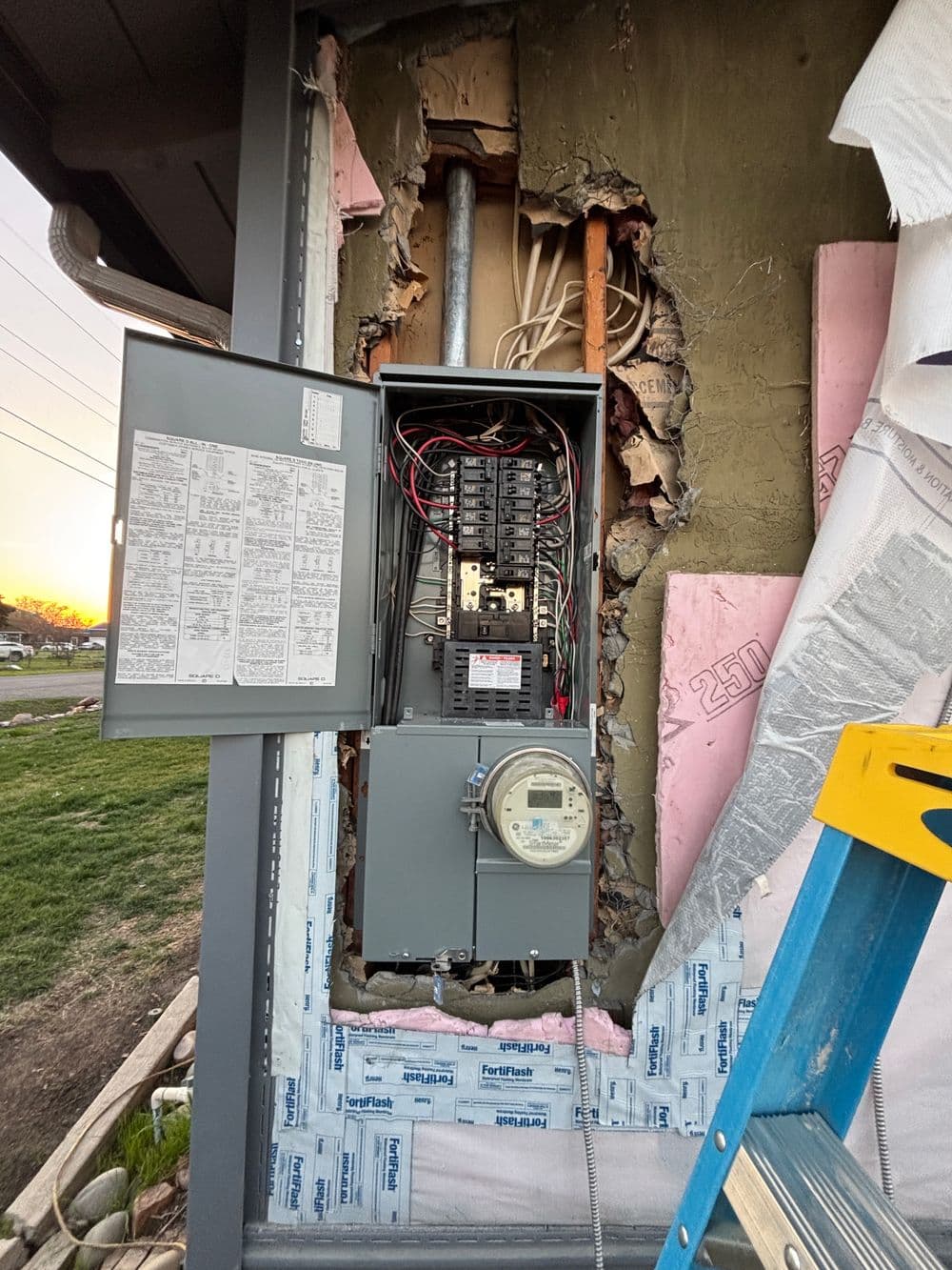 Electrical panel installation with exposed wall, wires, and ladder in residential setting.