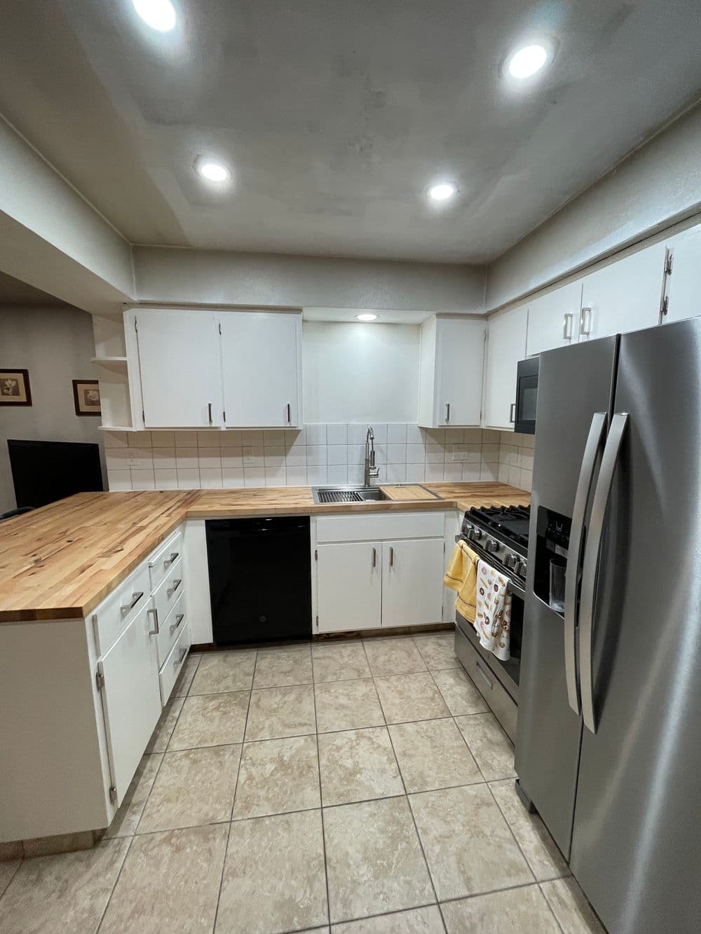 Modern kitchen with white cabinets, stainless steel appliances, and a wooden countertop.