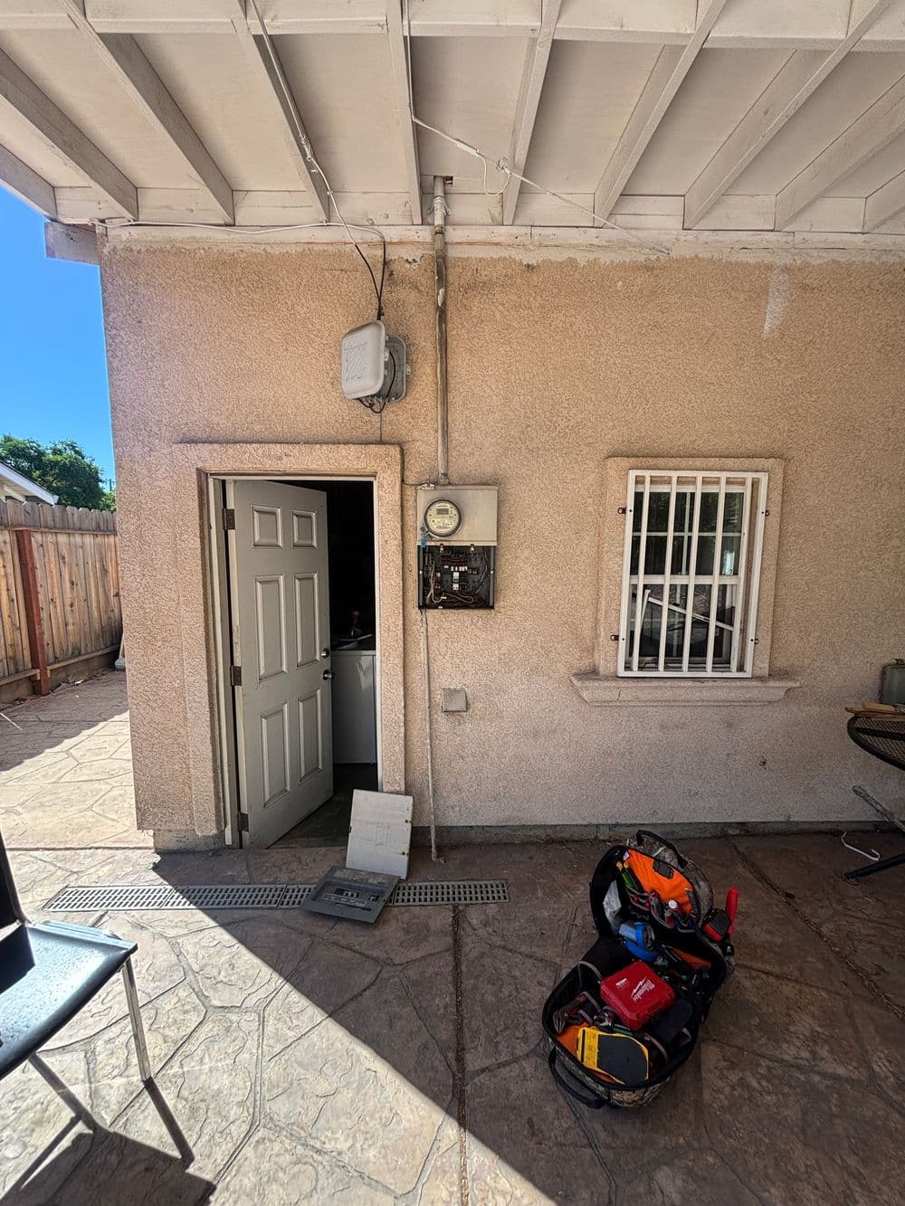 Exterior view of a home with electrical meter, door, and tools on a patio.