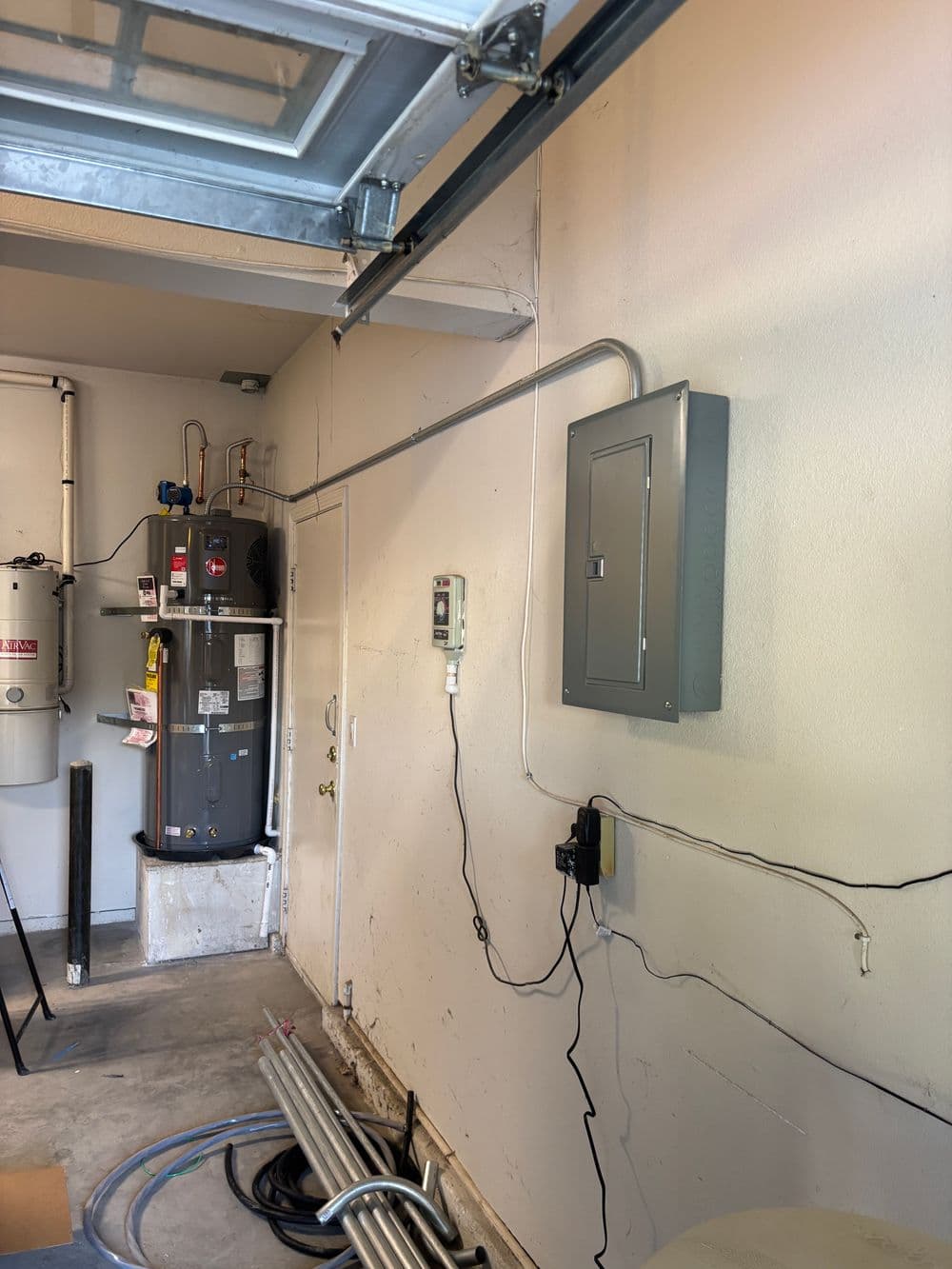 Garage interior featuring electrical panel, water heater, and exposed wiring.