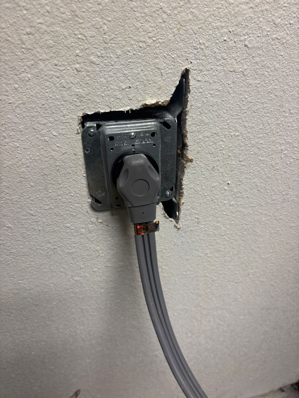 Electrical outlet with gray cable installed in a damaged wall section.
