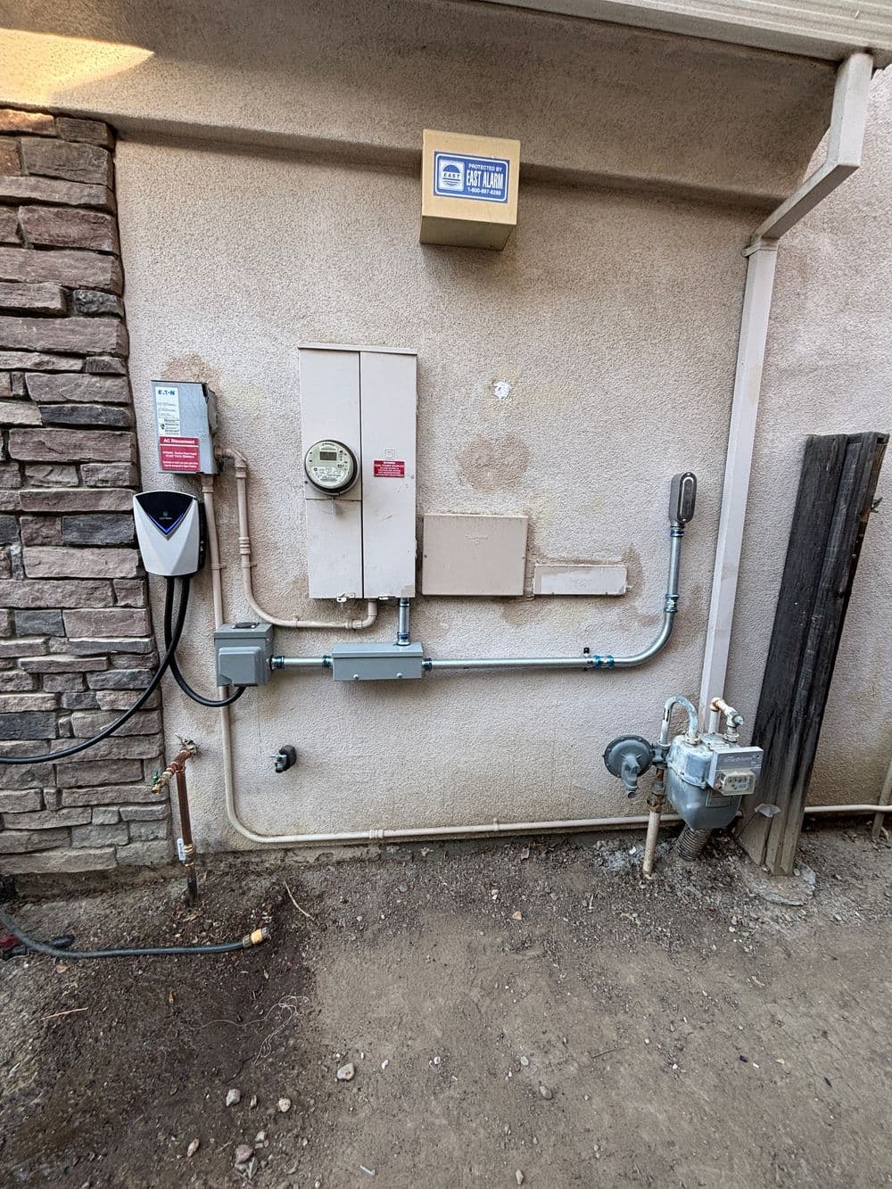 Gas meter and utility box on an exterior wall with stone accents and utility connections.